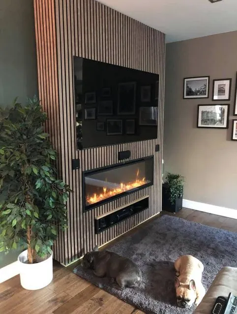 A floor-to-ceiling vertical slatted wood accent wall featuring a mounted flat-screen television directly above a sleek, modern linear electric fireplace.