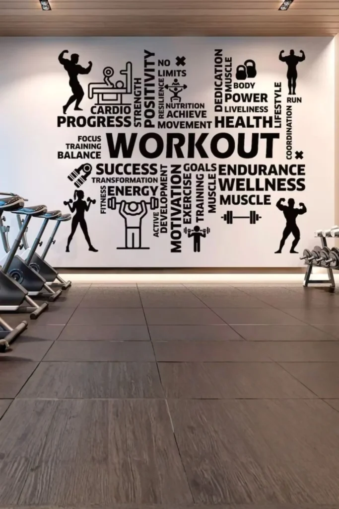 A spacious commercial or home gym facility featuring an expansive white accent wall covered in a large black typographic word cloud graphic with fitness motivation terms like "WORKOUT", "PROGRESS", and "WELLNESS" alongside minimalist exercise silhouettes, situated above dark tiled flooring next to stationary spin bikes.