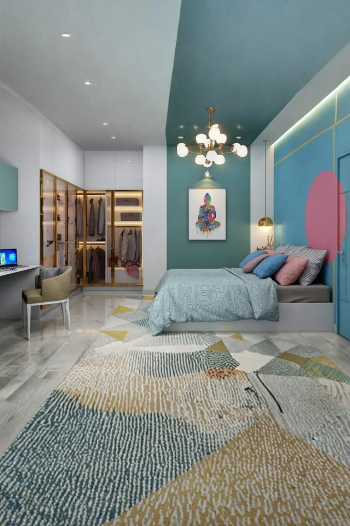 A modern, spacious bedroom layout demonstrating an integrated minimalist bedroom clothing storage system. The room features a bed styled with a light blue patterned duvet and pink accent pillows, set against a teal and blue geometric accent wall with a colorful Buddha art piece. A large, patterned area rug sits on the light flooring, leading to a built-in corner wardrobe unit in the background with sleek white doors and gold-trimmed glass panels that showcase organized hanging clothes under warm interior lighting.