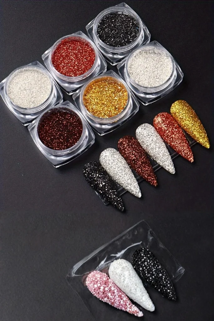 A high-angle shot showcasing small circular clear jars of fine loose glitters in gold, red, silver, bronze, and black shades arranged neatly on a dark background. Next to the jars, an array of almond-shaped nail tips completely coated in shimmering glitter is displayed, providing creative nail accessories design inspiration on how to categorize and view your shimmering palettes easily.