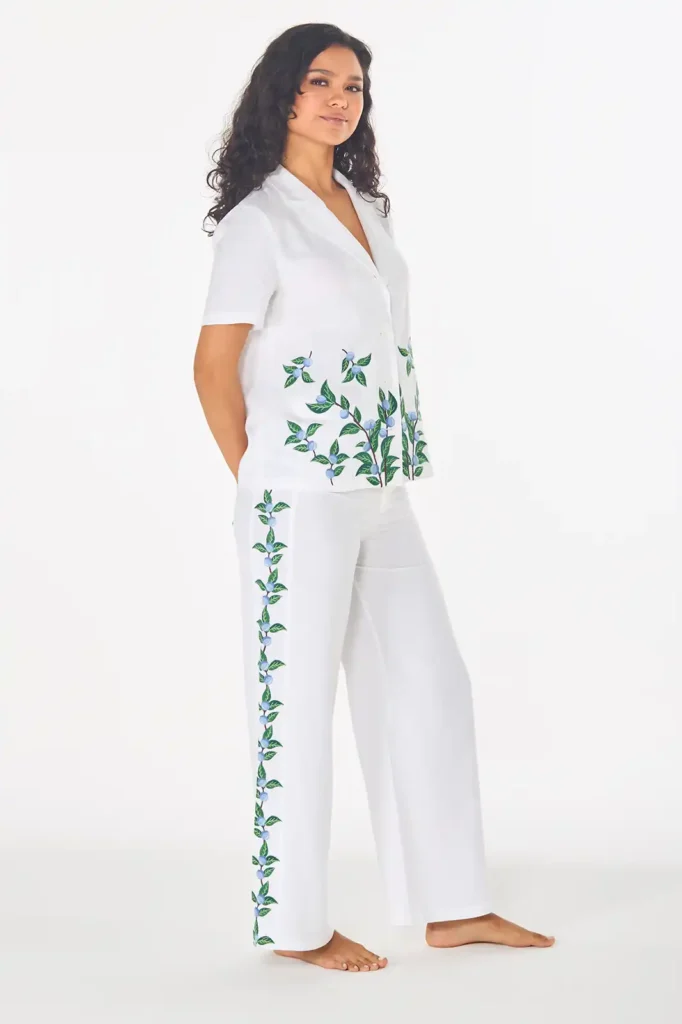 A woman posing in a matching linen co-ord set featuring a white short-sleeved shirt and wide-leg trousers with green leaves and blue berry embroidery, ideal for summer casual home outfits for women.