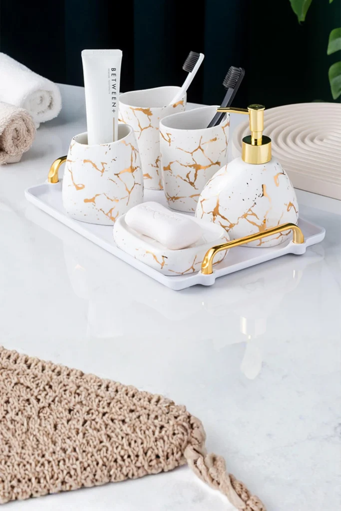 A luxury white ceramic bathroom vanity collection with striking gold marble veining, proving there is a reason the world's most luxurious hotels love stone finishes. Arranged beautifully on a matching tray with gold handles, this set shows how turning to a marble bathroom accessories inspiration aesthetic is the absolute easiest shortcut to making your home feel like a five-star spa. Investing in a matching marble liquid soap pump, toothbrush holder, and cotton jar set creates a clean, cohesive look that oozes luxury, complete with toothbrushes, toothpaste, and a bar of soap.