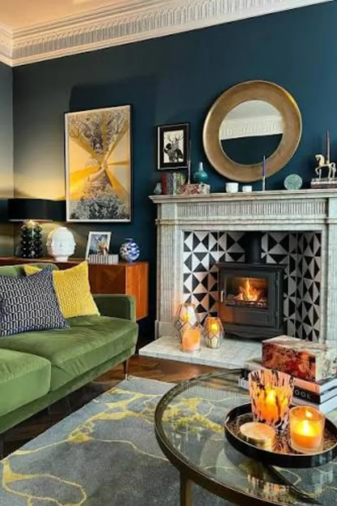 A moody living room showcasing victorian homes interior modern decorating ideas. Features include a classic fireplace mantle with black and white geometric tiled backing, a burning wood stove, a large round gold mirror, dark teal walls with intricate white crown molding, a green velvet sofa, and cozy warm lighting.