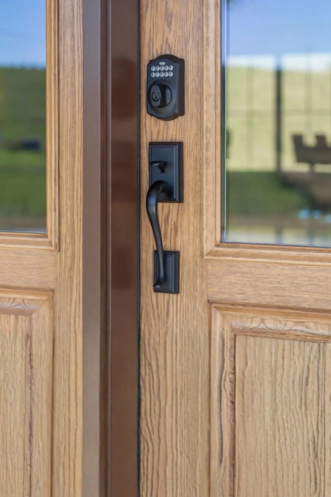 A close-up of a high-quality wood-grained front door featuring a modern black smart lock system installed above a matching black curved handle set. The electronic keypad deadbolt provides a Grade 1 or Grade 2 certified level of security, demonstrating that even the strongest door material needs secure hardware to protect your home from being easily bypassed or pried open.