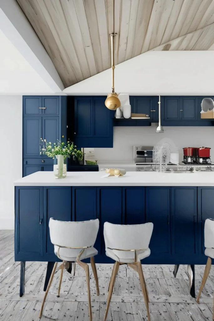 A striking modern kitchen featuring luxury navy blue accent wall ideas integrated into the full-height cabinetry and kitchen island. The space is complemented by a clean white countertop, elegant light gray bar stools with gold legs, a polished brass pendant light hanging from a vaulted wooden ceiling, and weathered light-colored flooring.