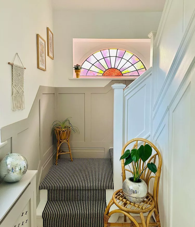 A colorful stained glass window in a sunburst pattern illuminating a staircase with a striped runner carpet, showing creative glass window ideas to add a surprise to a stairwell.