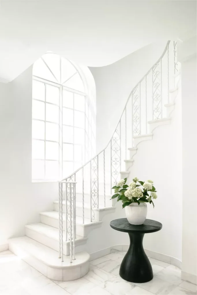 Elegant all-white wrought iron railing showcasing delicate, intricate indoor stair railing ideas in a bright, minimalist entryway.