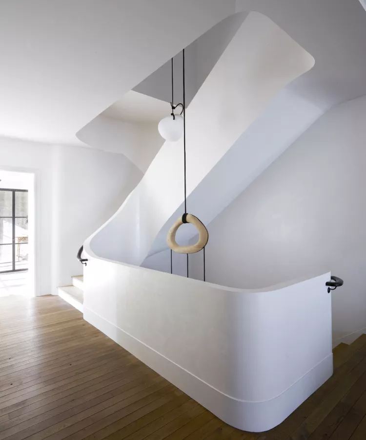 Elegant curved metal stair railings with sleek black handrails, showing modern, sculptural indoor stair railing ideas in a minimalist white foyer.