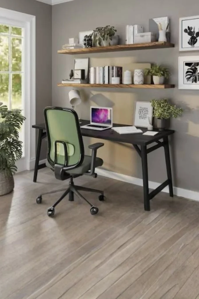 Modern home office setup featuring floating wooden shelves mounted above a black wooden desk, styled with organized books, potted plants, and framed artwork against a grey wall next to a green ergonomic office chair.