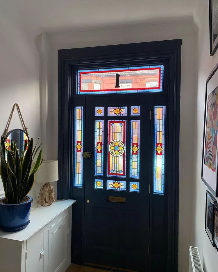 A heavy black front door surrounded by elaborate geometric stained glass panel sidelights and a matching numbered transom window, showing how stunning windows can incorporate a highly practical structural entry element while keeping a secure, balanced look.