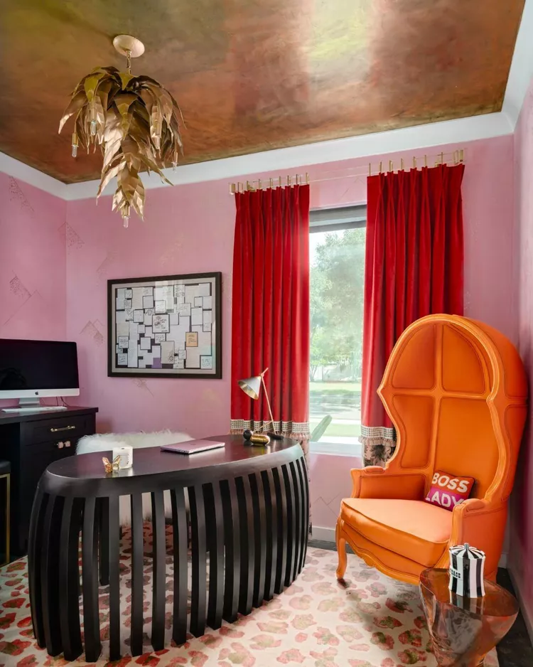 A bold, maximalist home office featuring pink walls, rich red velvet curtains, a high-back orange accent chair, and a striking textured metallic gold plaster ceiling, showcasing how aesthetic false ceiling ideas gracing beautiful decor of modern office designs can bring high-end energy and luxury to a creative workspace.