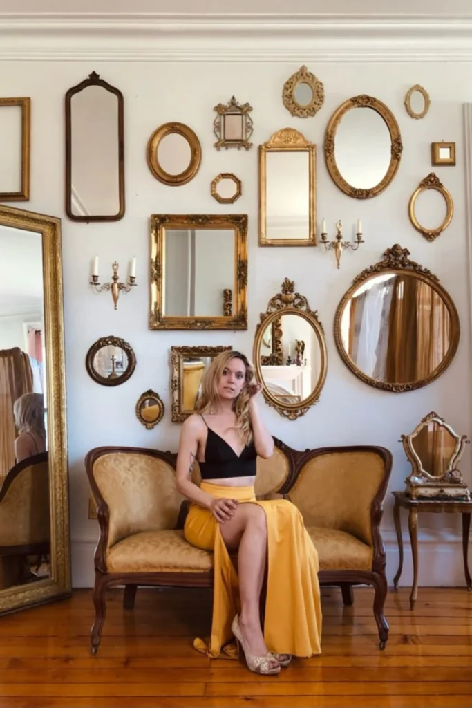 An artistic gallery wall featuring vintage ornate gold Mirror Collages of various shapes and sizes arranged above a mustard yellow vintage settee sofa.