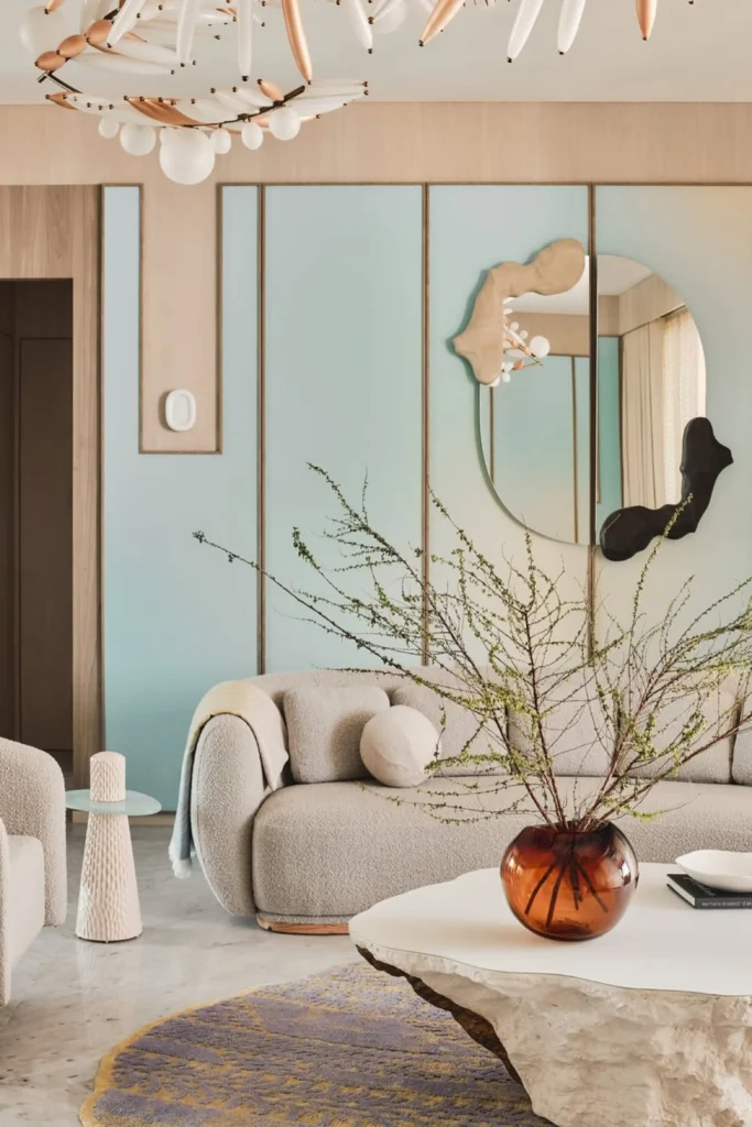 A modern living room featuring artistic Mirror and Artwork Combinations with an asymmetrical split circular mirror and organic wall sculptures mounted on light blue wall paneling behind a plush bouclé sofa.