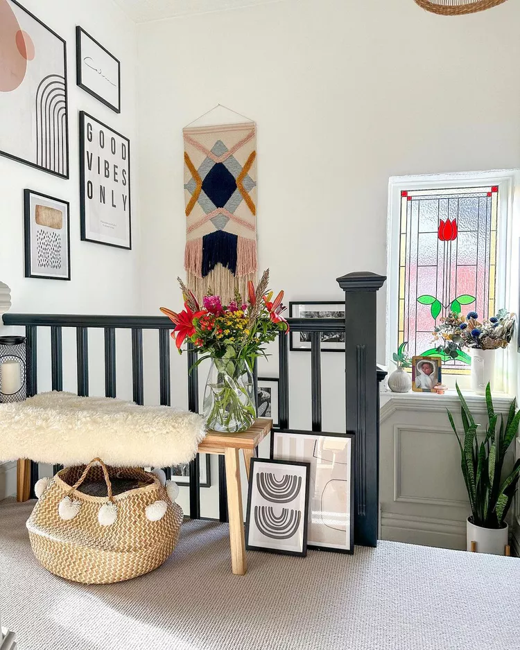 A beautifully styled landing area featuring an intricate tulip stained glass window that coordinates harmoniously with eclectic wall art, a woven wall hanging, and cozy boho textures, showcasing glass window ideas to play off your glass design.