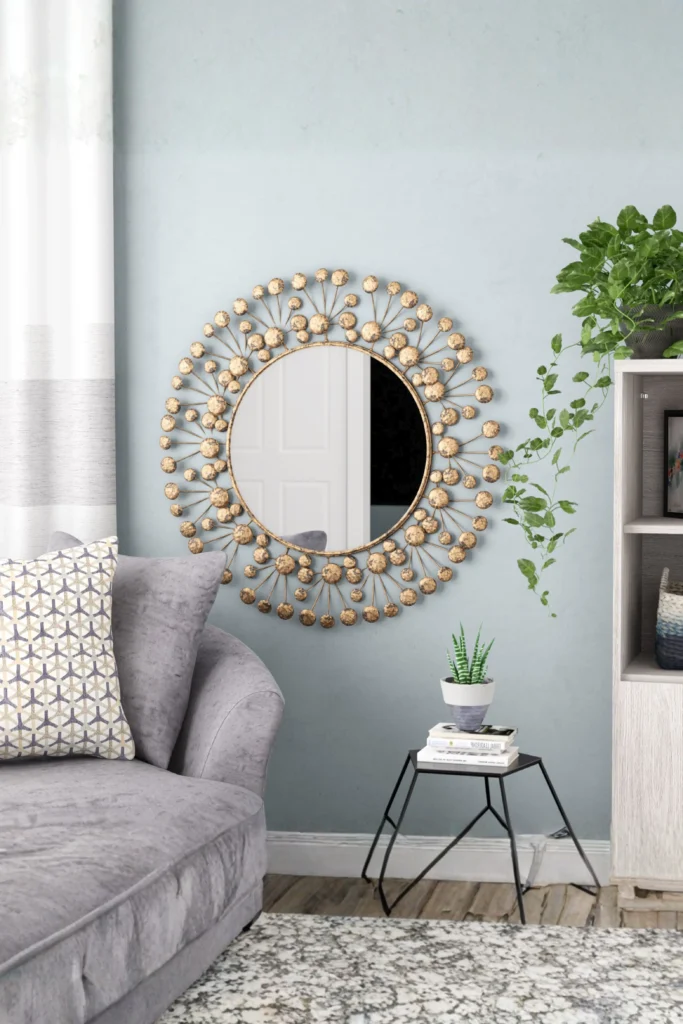 A stylish living room featuring a gold sunburst-style Round Accent Mirror mounted on a light blue wall above a grey sofa and a black side table.