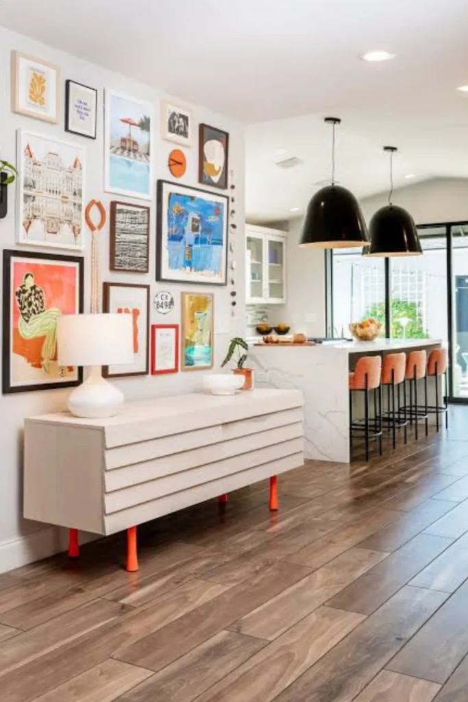 A stylish open-concept living area featuring a colorful floor-to-ceiling art gallery wall display above a light wood console table with bright orange legs, showcasing creative Apartment Rooms ideas to personalize rental spaces.