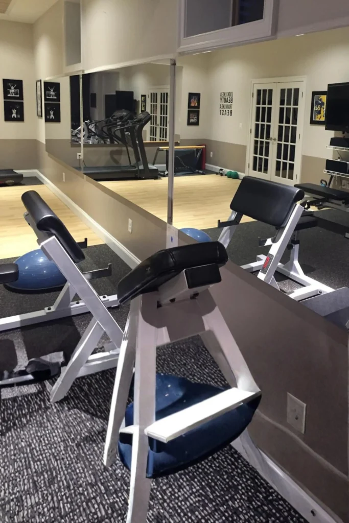 A spacious home gym featuring large frameless wall-to-wall mirrors mounted above the wall trim, reflecting workout equipment like exercise benches, a treadmill, and a Bosu ball.