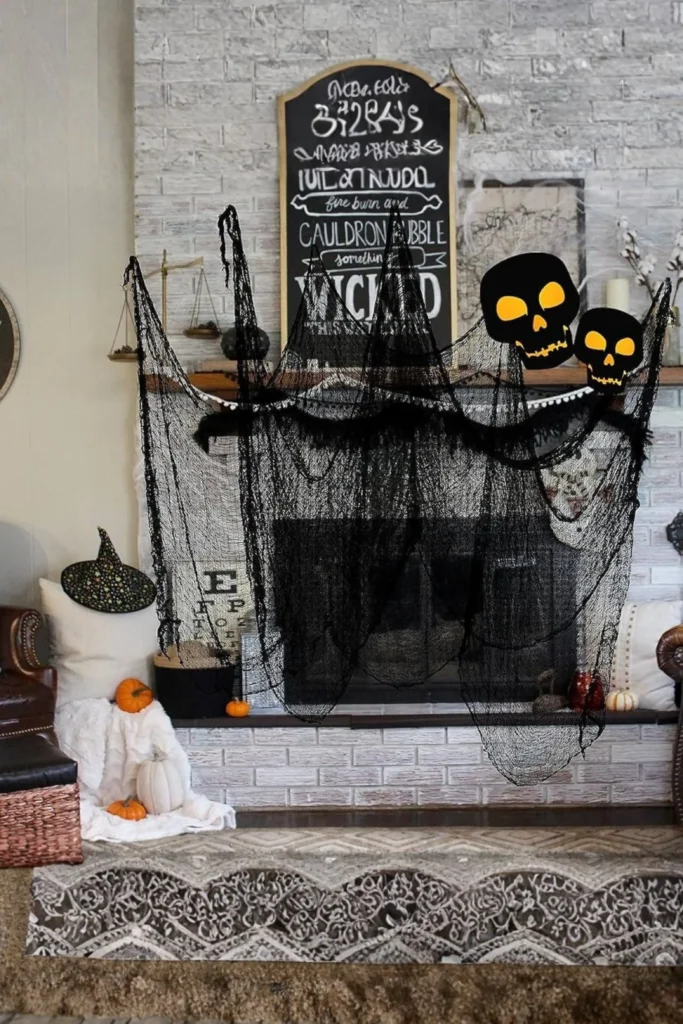 Distressed black creepy cloth draped across a brick fireplace mantel for Halloween, accented with yellow-eyed skull graphics, pumpkins, and a chalkboard spell sign.