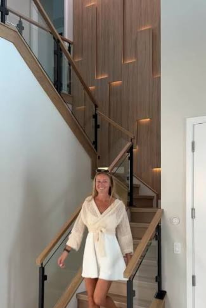 Modern staircase with a multi-dimensional wood slat accent wall featuring integrated warm LED backlighting and glass railings.