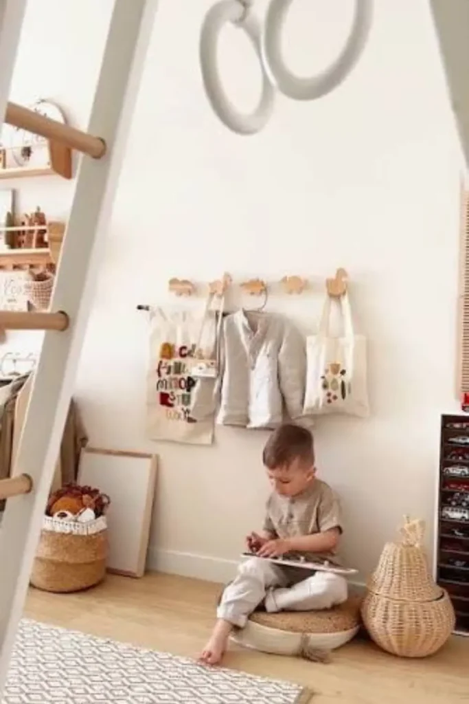 Low-mounted wooden wall pegs & hanging hooks shaped like animals in a toddler room holding a child's jacket, tote bags, and alphabet wall hanging.